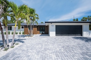 Ein modernes Haus mit Garage, gepflasterter Auffahrt und Palmen.