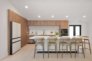 Eine moderne Küche mit Holzschränken, einer zentralen Kochinsel mit Barhocker, einem Kühlschrank und einem Backofen.