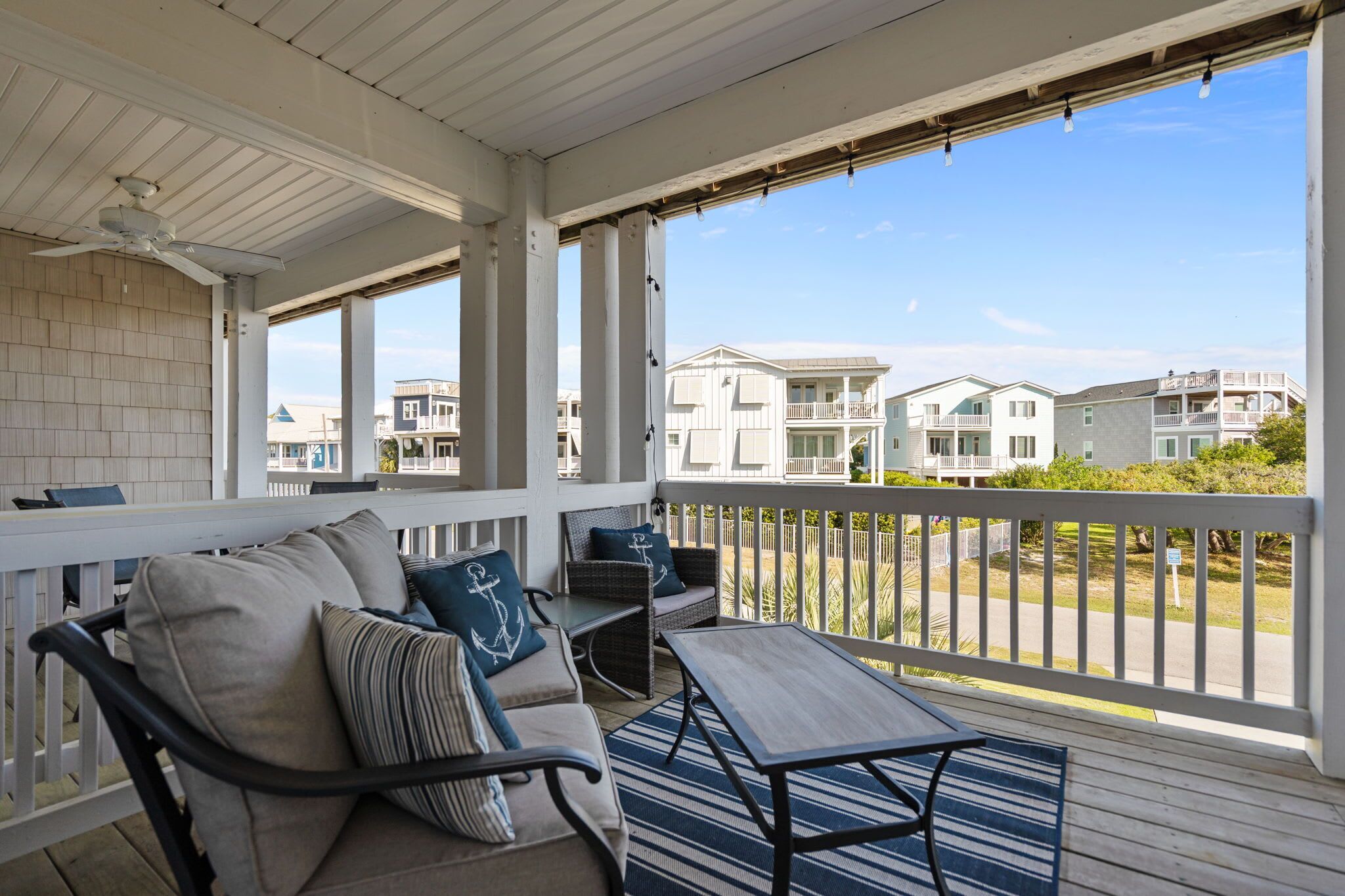 A covered porch with outdoor furniture, a ceiling fan, and a view of neighboring houses.