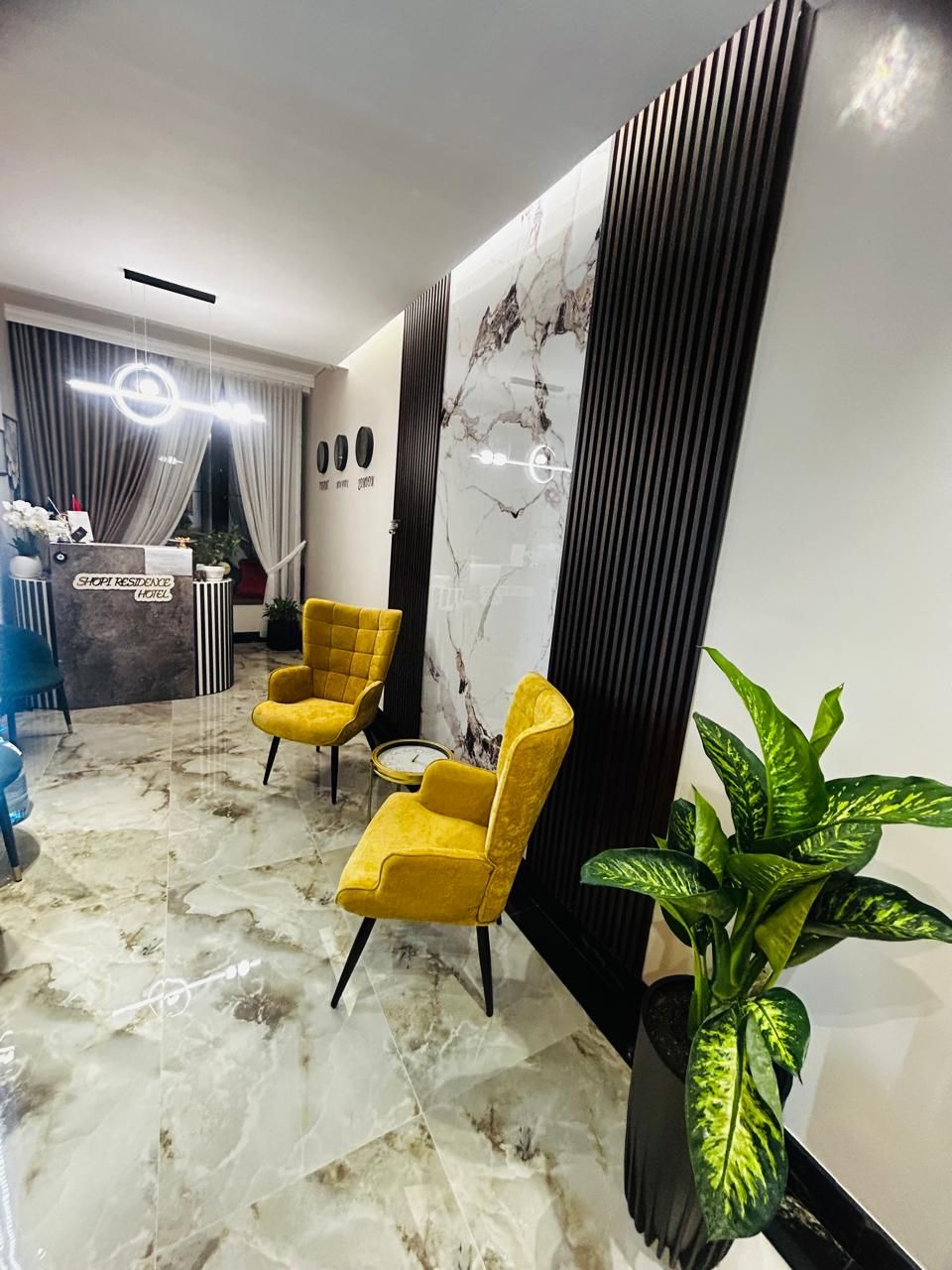 A reception area with a marble floor, two yellow chairs, a reception desk, and a large potted plant.