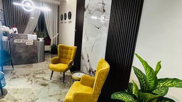 A reception area with a marble floor, two yellow chairs, a reception desk, and a large potted plant.