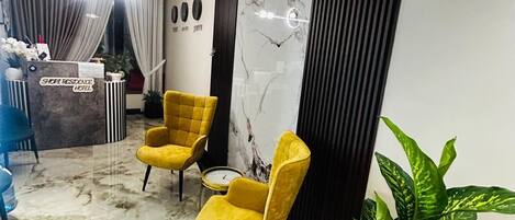 A reception area with a marble floor, two yellow chairs, a reception desk, and a large potted plant.