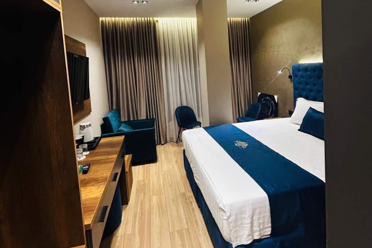 A hotel room with a bed, a desk, a chair, a TV, and a window with curtains.