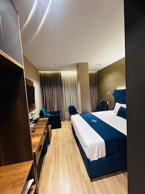 A hotel room with a bed, a desk, a chair, a TV, and a window with curtains.
