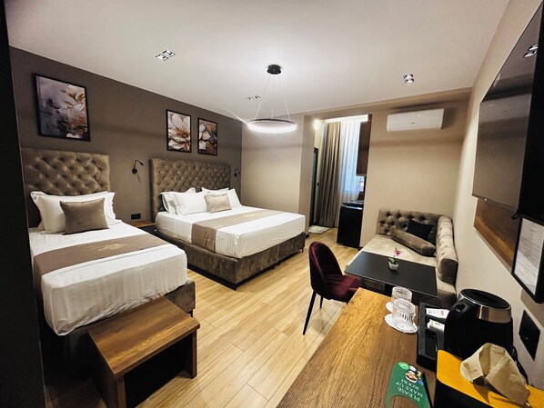 A hotel room with two beds, a sofa, a dining table, and a small kitchen area.