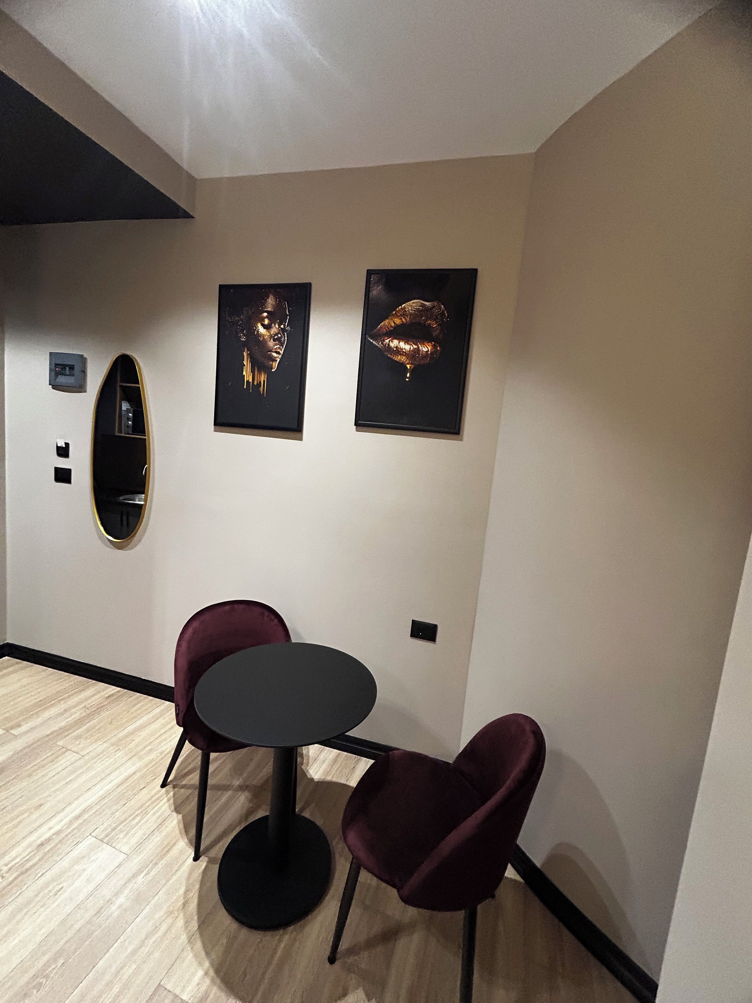 Una habitación con una mesa redonda y dos sillas, un espejo ovalado fijado a la pared, y dos obras de arte enmarcadas.