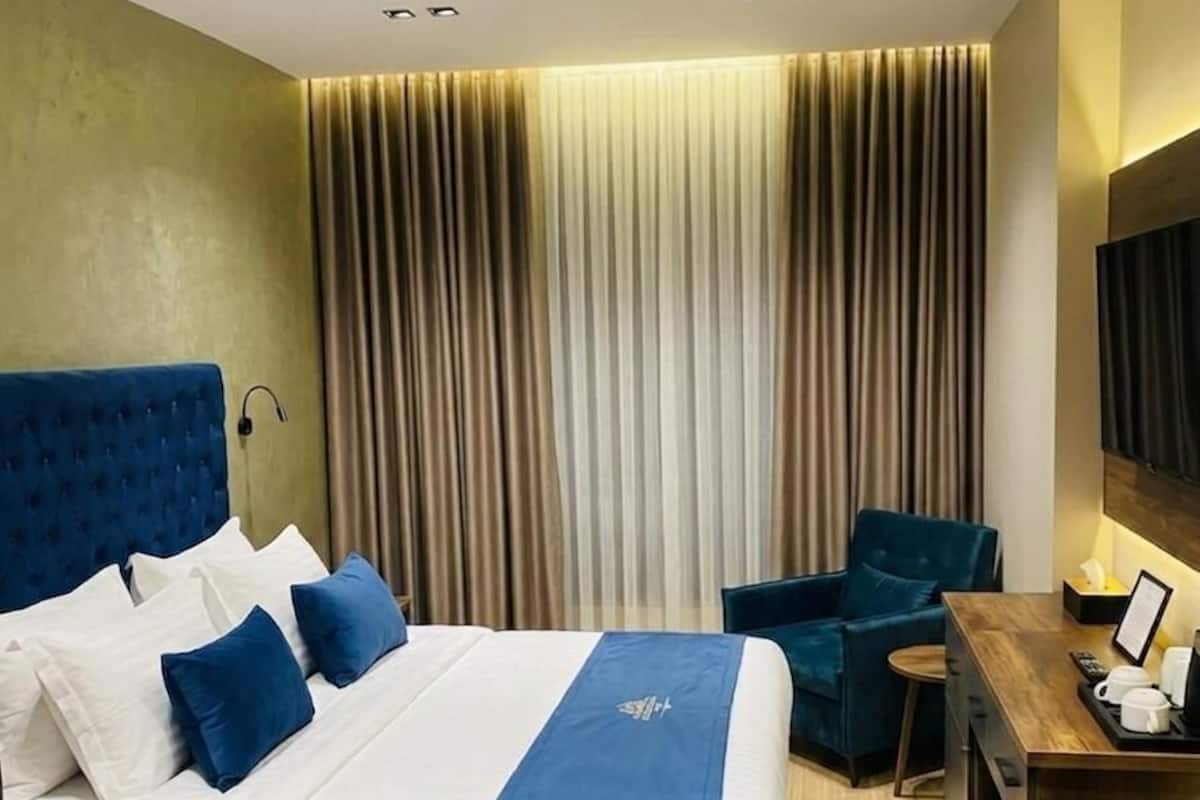 A hotel room with a large bed, a desk, a chair, and a TV.