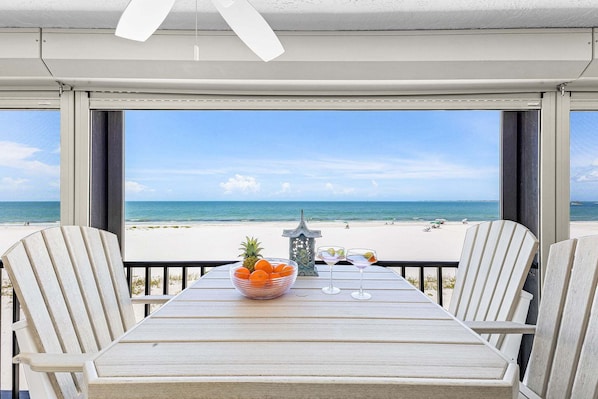 A table with a bowl of fruit and two glasses, overlooking a beach. - Beachfront Sunsets, Heated Pool & Gulf Views Escape - Dolphin Watch 203 - Roelens (Fort Myers Beach)