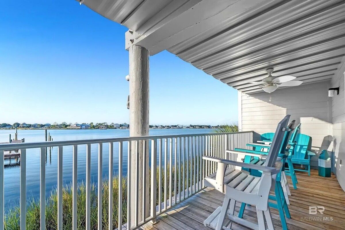 A wooden deck with a railing overlooking a body of water, a ceiling fan, and outdoor furniture.