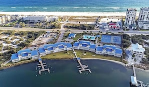 An aerial view of a coastal hotel with multiple buildings, a dock, and a beach in the background. - A14 Sundown Riverside Condominiums (Perdido Key)