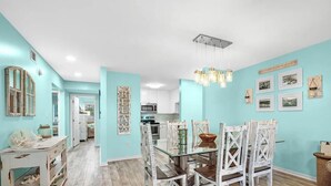 A modern kitchen with white cabinets, a dining area with a glass table, and a light blue wall. - A14 Sundown Riverside Condominiums (Perdido Key)