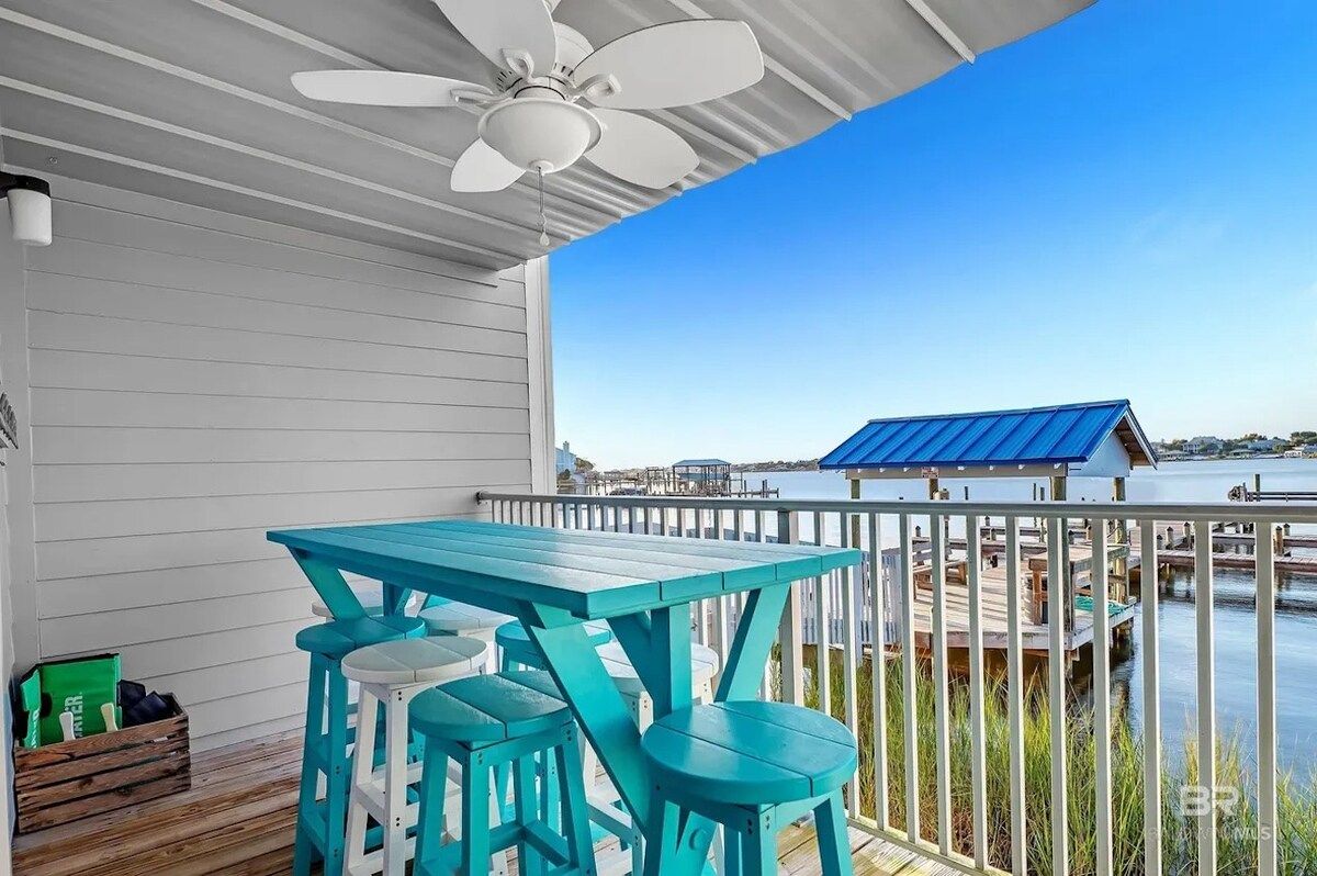 A covered outdoor area with a table and chairs, a ceiling fan, and a view of a dock and water.