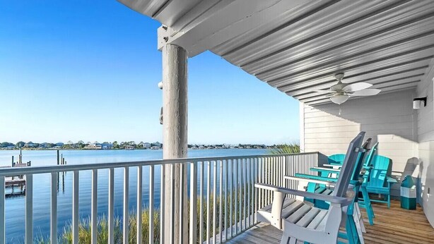 A wooden deck with a railing overlooking a body of water, a ceiling fan, and outdoor furniture. - A14 Sundown Riverside Condominiums (Perdido Key)