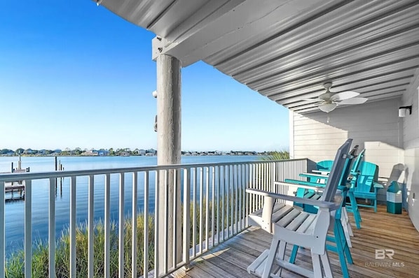 A wooden deck with a railing overlooking a body of water, a ceiling fan, and outdoor furniture. - A14 Sundown Riverside Condominiums (Perdido Key)