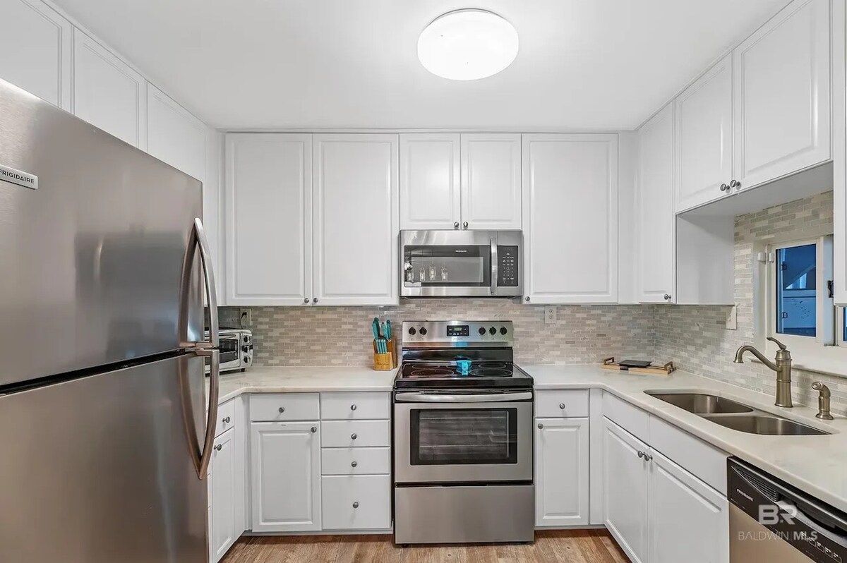 A modern kitchen with white cabinetry, stainless steel appliances, and a tiled backsplash.