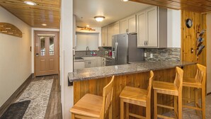 A modern kitchen with wooden bar stools, stainless steel appliances, and a stone backsplash. - NEW! Ski. Hike. Fish. Big Sky Mountain Village (Big Sky)