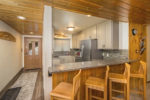 A modern kitchen with wooden bar stools, stainless steel appliances, and a stone backsplash. - NEW! Ski. Hike. Fish. Big Sky Mountain Village (Big Sky)