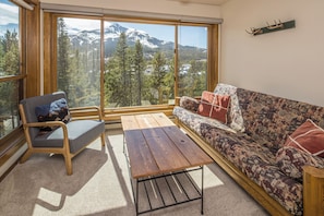 A room with a wooden bench, a sofa, and a large window offering a mountain view. - NEW! Ski. Hike. Fish. Big Sky Mountain Village (Big Sky)