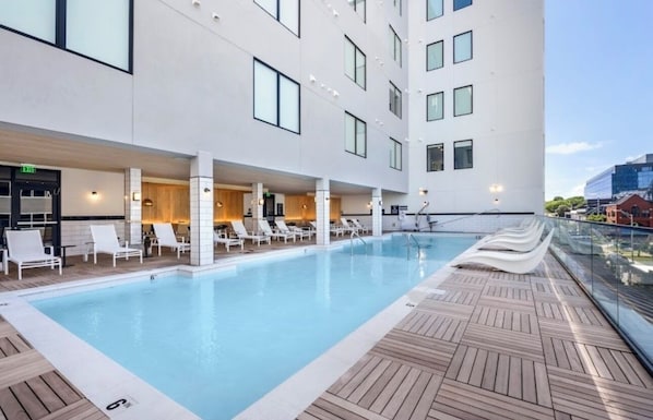 Ein modernes Hotel mit Pool auf dem Dach, Liegestühlen und einer Glasumlaufung mit Blick auf die Stadt.