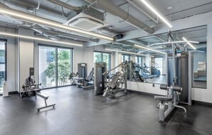 A modern gym with various exercise machines, large windows, and a clean, industrial design.