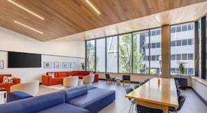 A modern interior with a wooden ceiling, large windows, a blue sofa, a red sofa, and a wooden table.