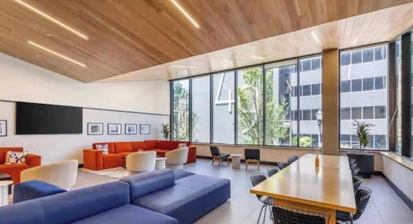 Un intérieur moderne avec un plafond en bois, de grandes fenêtres, un canapé bleu, des fauteuils orange et une table en bois.