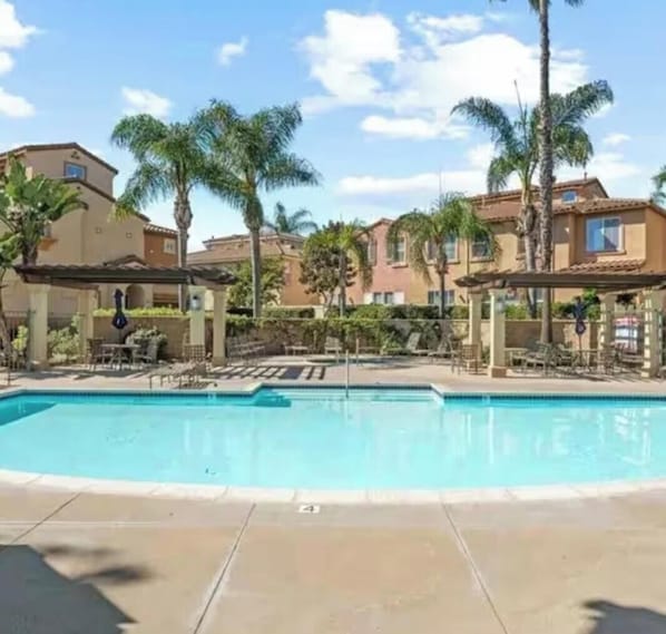 A swimming pool with lounge chairs and palm trees, surrounded by buildings.