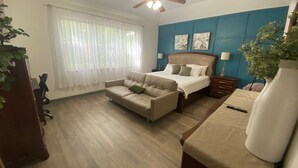Un dormitorio con cama, sofá, escritorio, ventilador de techo y ventana con cortinas.