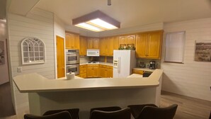 Una cocina con armarios de madera, un refrigerador blanco, un microondas, un horno e isla integrada con taburetes de bar.