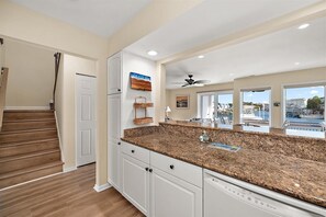A kitchen with granite countertops, white cabinetry, a dishwasher, and a view of the marina through large windows. - Canal-Front Coastal Retreat w/ Water Views, Walk to Beach (Ocean City)