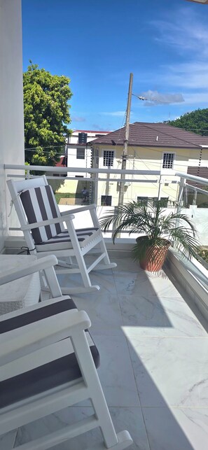 A balcony with white rocking chairs and a potted plant. - 3-bedroom apartment in charming Puerto Plata with AC (Puerto Plata)
