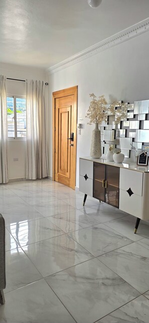 A room with a wooden door, a white cabinet with decorative elements, a vase with flowers, and a window with curtains. - 3-bedroom apartment in charming Puerto Plata with AC (Puerto Plata)