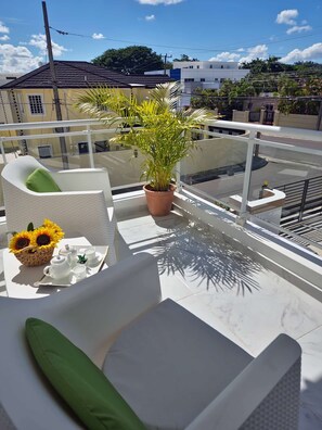 Un balcone con un divano bianco, una pianta in vaso e un vassoio con decorazione a girasole e teiera.