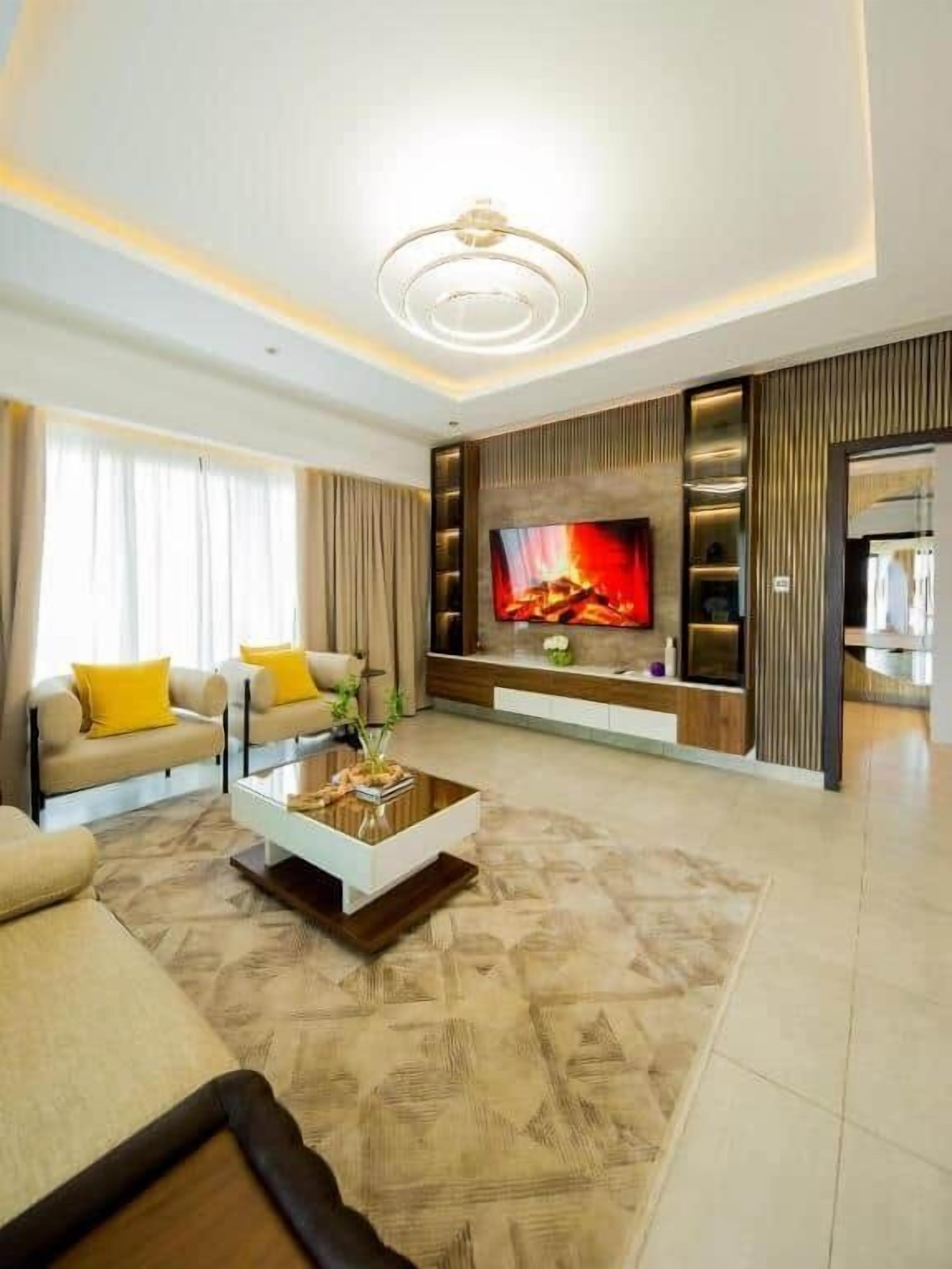 A modern living room with a flat-screen TV, a sofa set, a coffee table, and a patterned rug.