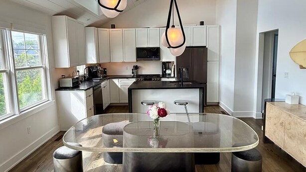 Une cuisine moderne avec des meubles blancs, un îlot central doté de sièges et des luminaires suspendus.