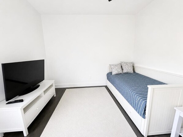 Una camera da letto con un letto, una TV su un mobile bianco e una cassettiera bianca.