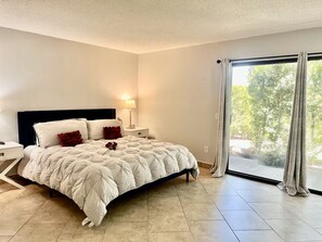 Ein Schlafzimmer mit Bett, Nachttisch, Lampe und Blick durch ein großes Fenster.
