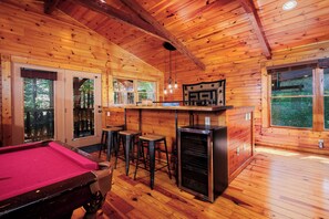 Ein Holzblockhaus-Interieur mit Billardtisch, Bar und Kamin.
