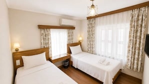 A hotel room with two beds, a wooden headboard, an air conditioning unit, a nightstand, a lamp, and a television. - Nisa Pansiyon (Ayvalık)
