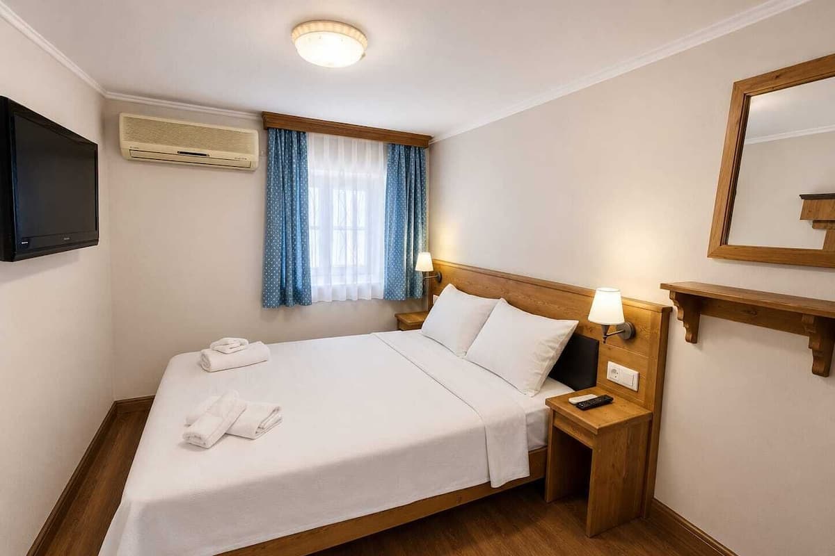 Una habitación de hotel con cama, lámparas de noche, televisión, espejo y ventana con cortinas.