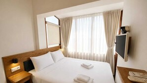 A hotel room with a bed, a TV, a bedside table, and a window with curtains. - Nisa Pansiyon (Ayvalık)