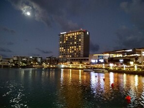 A waterfront hotel with multiple floors, a marina with boats, and a city skyline in the background. - Fun & relax suite beside a park, 10 min to beaches (Cancún)