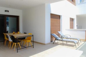 A modern outdoor dining area with a table and chairs, a poolside lounge area, and a sliding door.