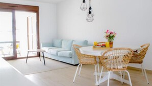 Een moderne woonkamer met een lichtblauwe bank, een ronde eettafel met rieten stoelen, een klein bijzettafeltje en een potplant.