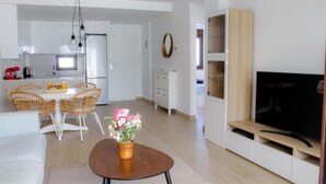 Een moderne woonkamer met een bank, een salontafel en een televisie. Er is een eethoek met een tafel en stoelen.