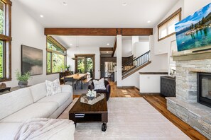 Ein geräumiges Wohnzimmer mit Sofa, Couchtisch und Kamin. Es gibt einen Essbereich mit Tisch und Stühlen, und im Hintergrund eine Küche.