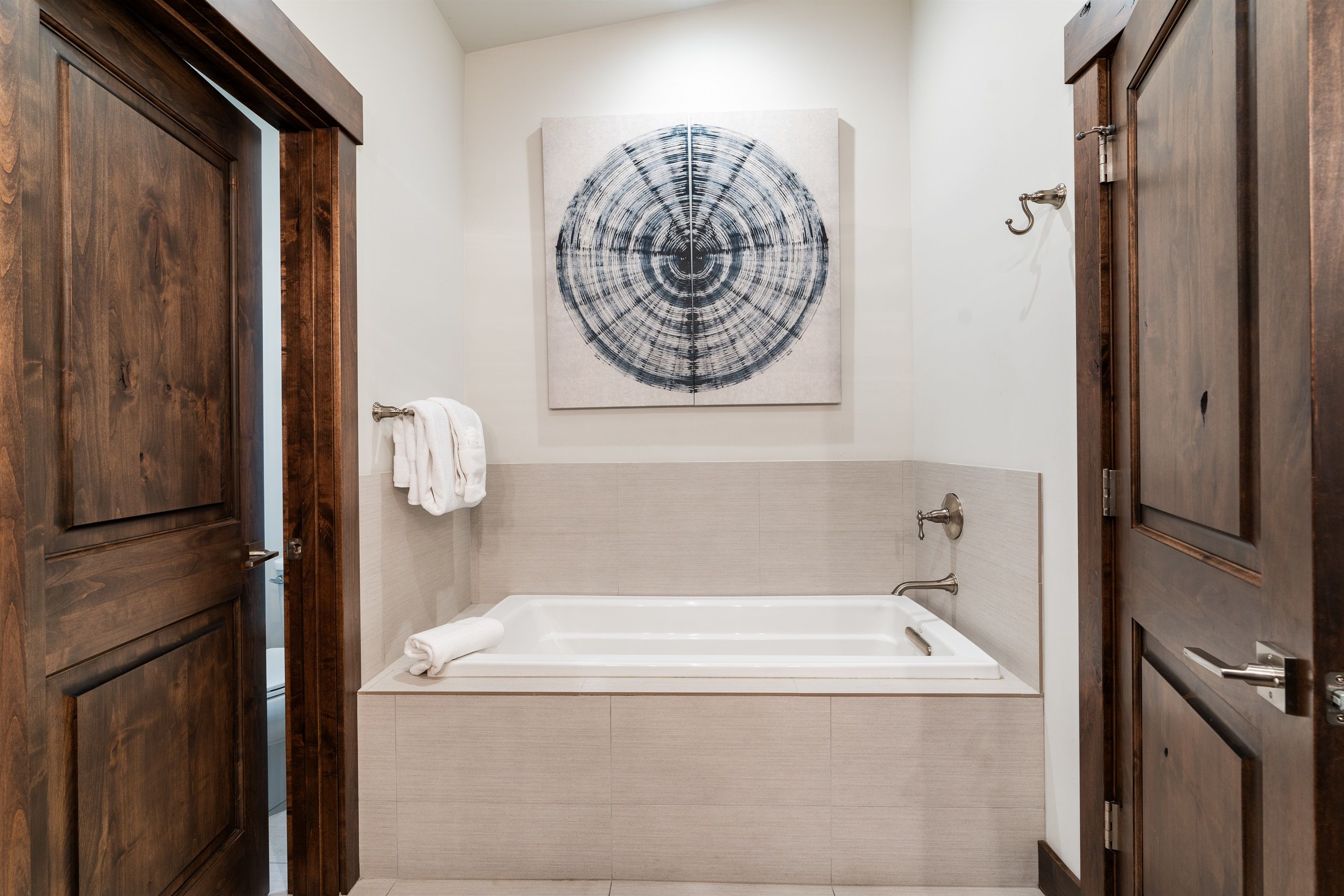 Une salle de bain avec une baignoire, des portes en bois, un porte-serviettes et une œuvre d’art accrochée au mur.