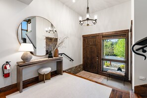 A bathroom with a large mirror, a round table, a bench, a chandelier, and a wooden door. - Newly Redesigned Tahoe Retreat | Private Hot Tub (Truckee)