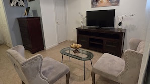 Uma sala de estar com dois poltronas, uma mesa de centro, uma televisão e obras de arte na parede.