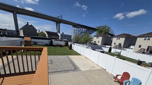 Um quintal com deck de madeira, um pátio de concreto e cerca branca.